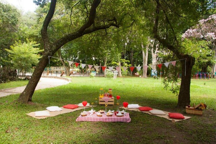 Na imagem, ambiente aberto com árvores e gramado decorados para uma festa de aniversário