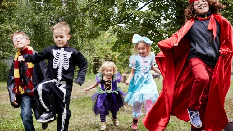 Crianças vestindo fantasias de Halloween correndo em lugar gramado