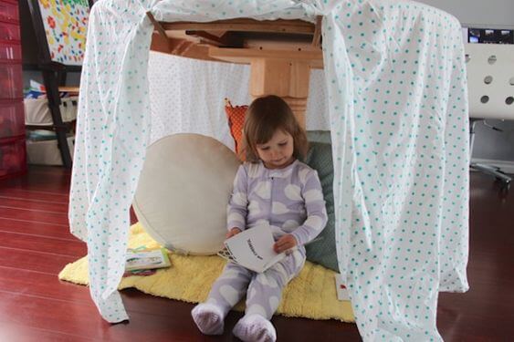 Menina dentro de uma cabana de lençóis