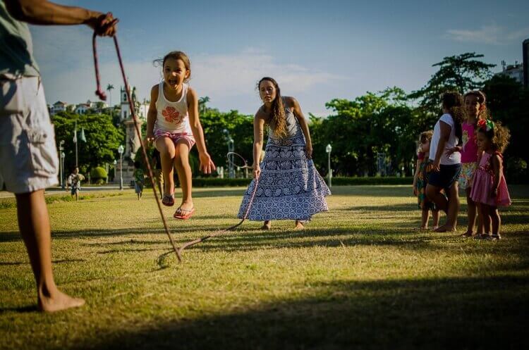 Criança feliz pulando corda segurada por uma mulher e por um homem em um parque