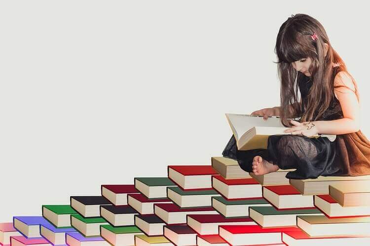 Menina sentada em cima de livros e lendo um livro.